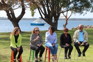 Four women and one man sitting on stools outdoors as part of a panel discussion