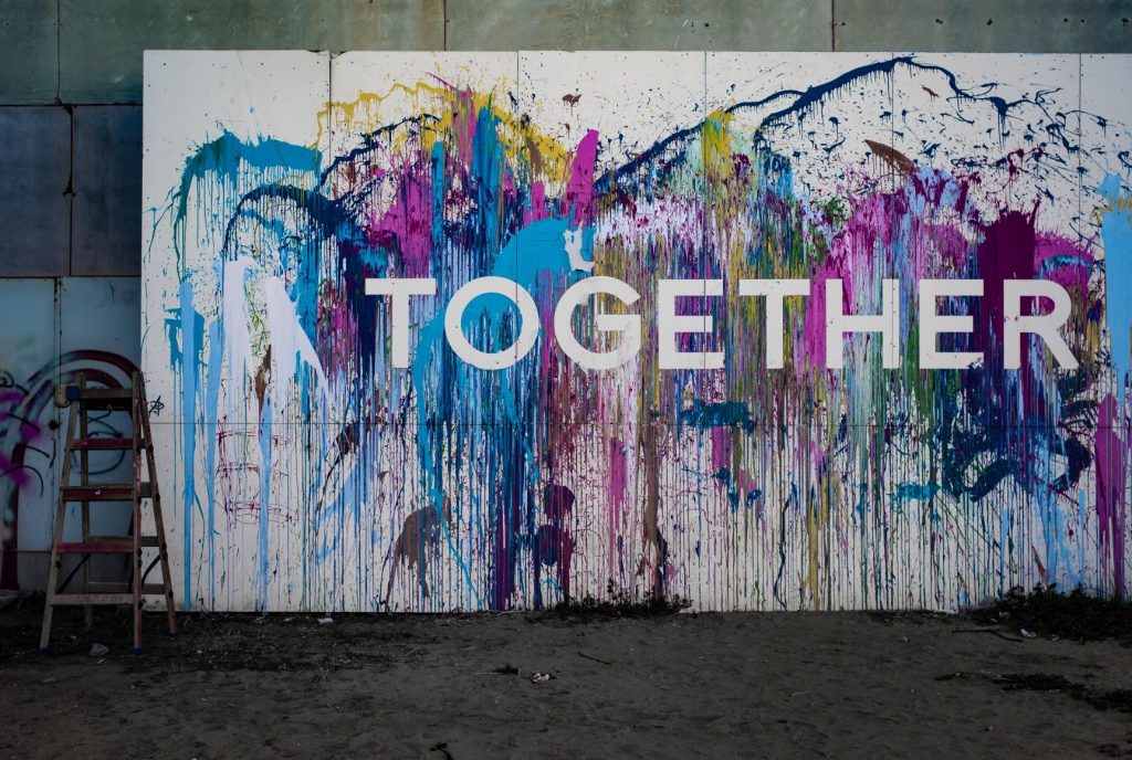 A white canvas with multi-coloured splashes of paint. The word together is across the canvas in capital letters.