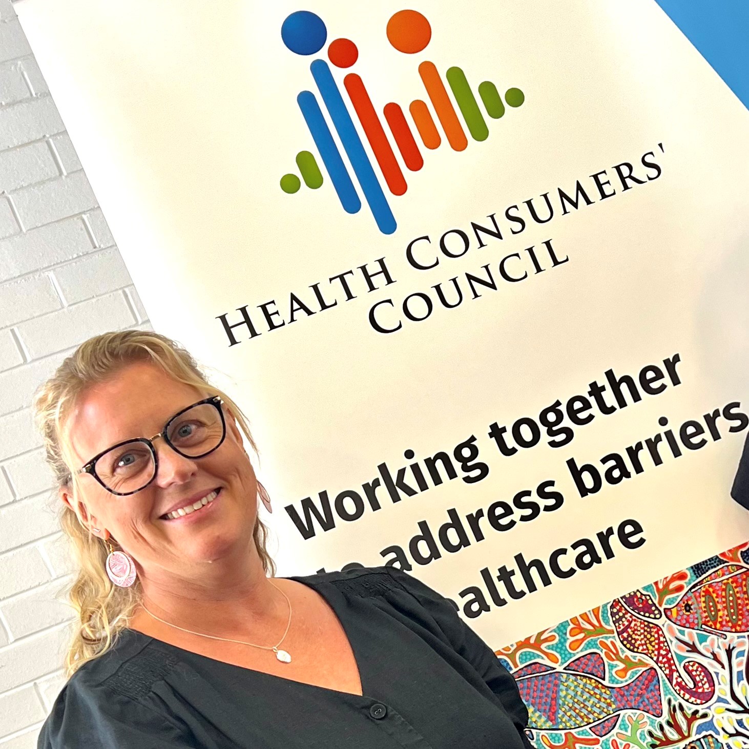 Suzanna Robertson, executivedirector of Health Consumers' Council, head and shoulders pictured to the left of a branded banner with logo and tagline that reads "Health Consumers' Council, working together to address barriers in healthcare".