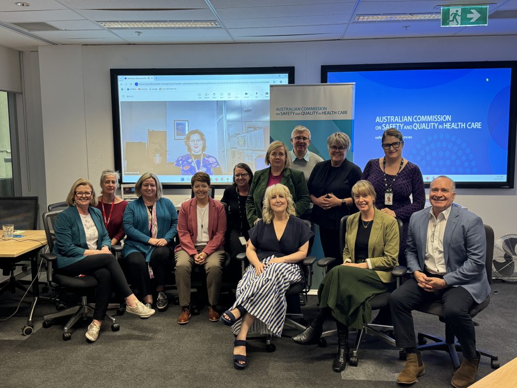 A group image with 12 people in the room and one person on the screen.